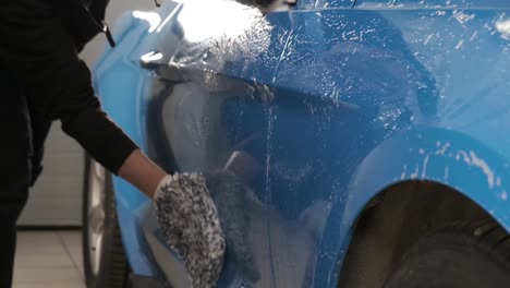 men's hand in blue gloves washing a car.