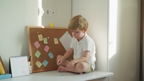 niño descalzo examina un pedazo de papel con un alfiler que sostiene la nota