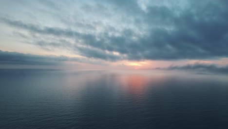 fixed drone view of pink sunset over open blue water with dark clouds stretching to the horizon