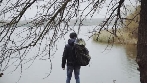 man standing near river. young man with backpack walking near the river in autumn season