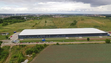aerial panorama of a modern plant. exterior of a large commercial warehouse situated among green fields. camera moves forward.