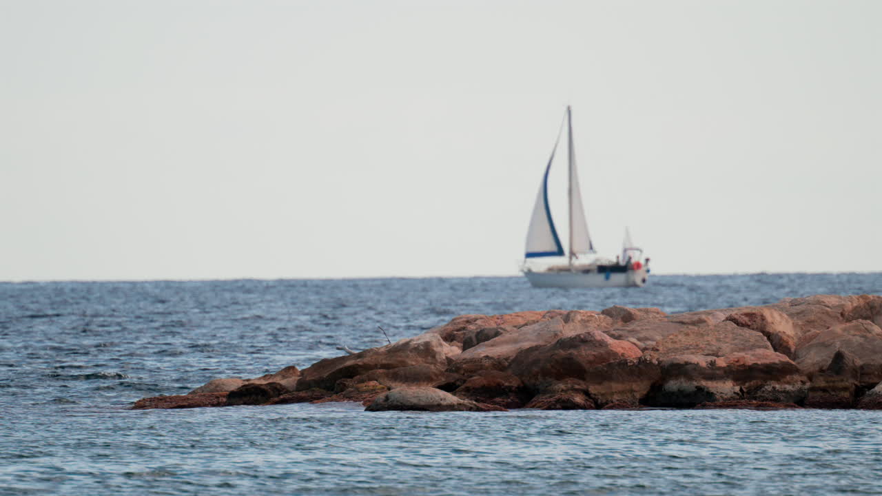A sailboat glides in the distance behind rocky coastal formations