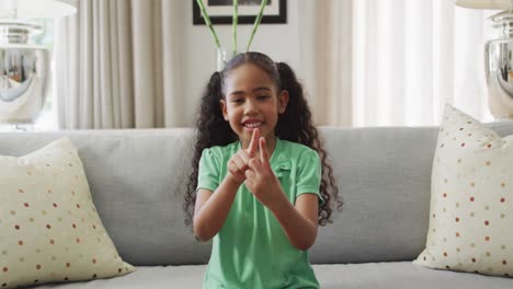 Happy-biracial-girl-sitting-on-sofa-using-sign-language