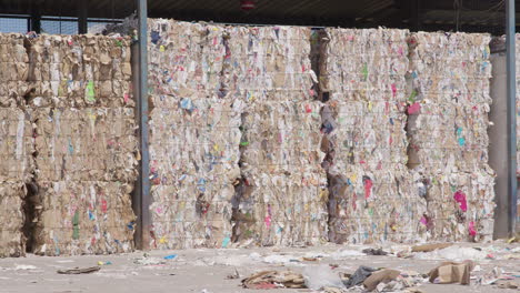 Large-paper-bales-stacked-at-outdoor-recycling-plant,-wide-slow-pan