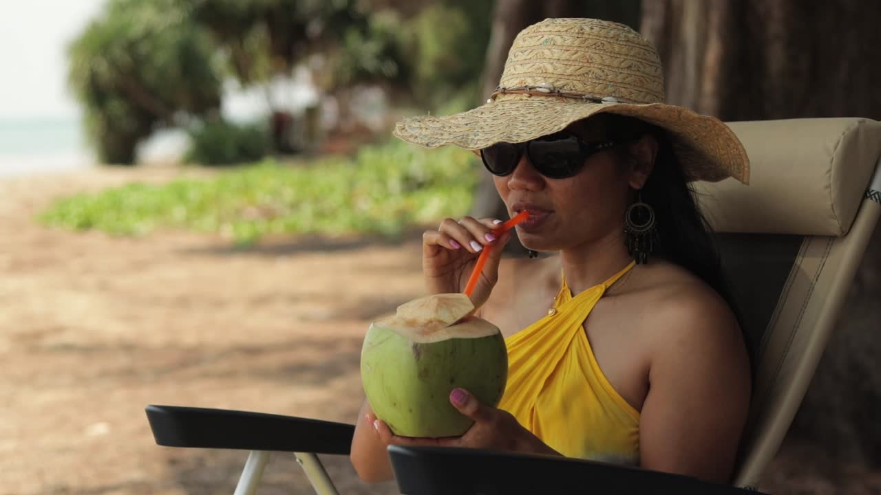 chica asiática bebiendo jugo de coco fresco en la costa tropical