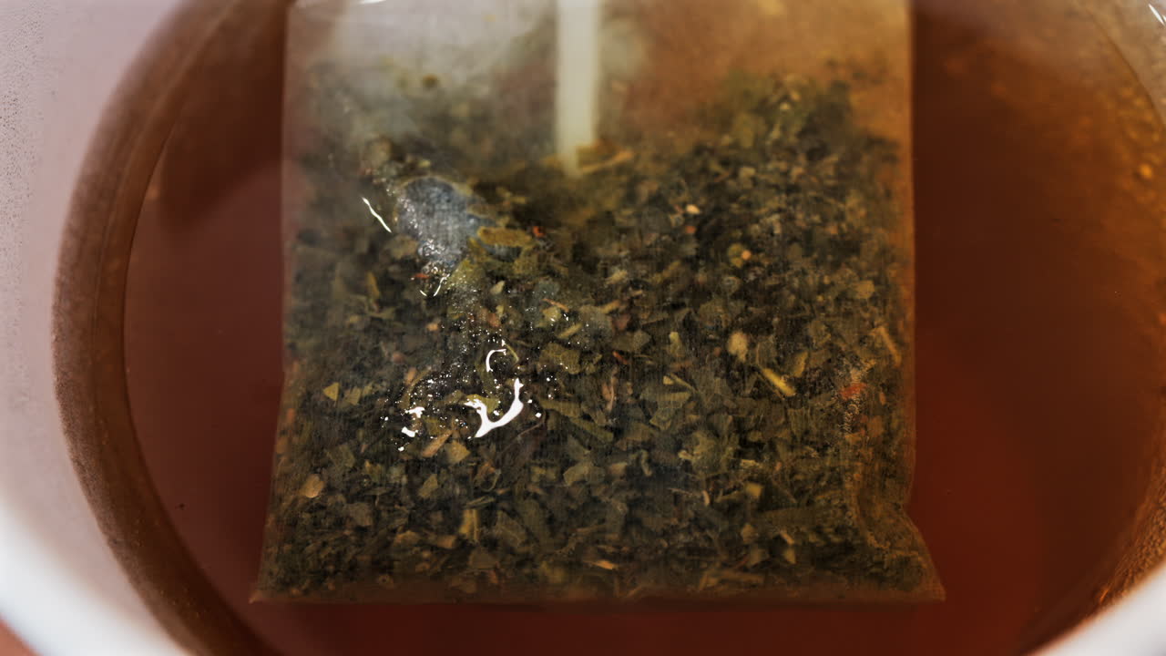 Close up of a tea bag brewing into a red cup