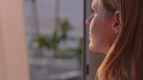 young woman opening curtain enjoying early morning sunrise looking at beautiful view with golden sunlight revealing new day