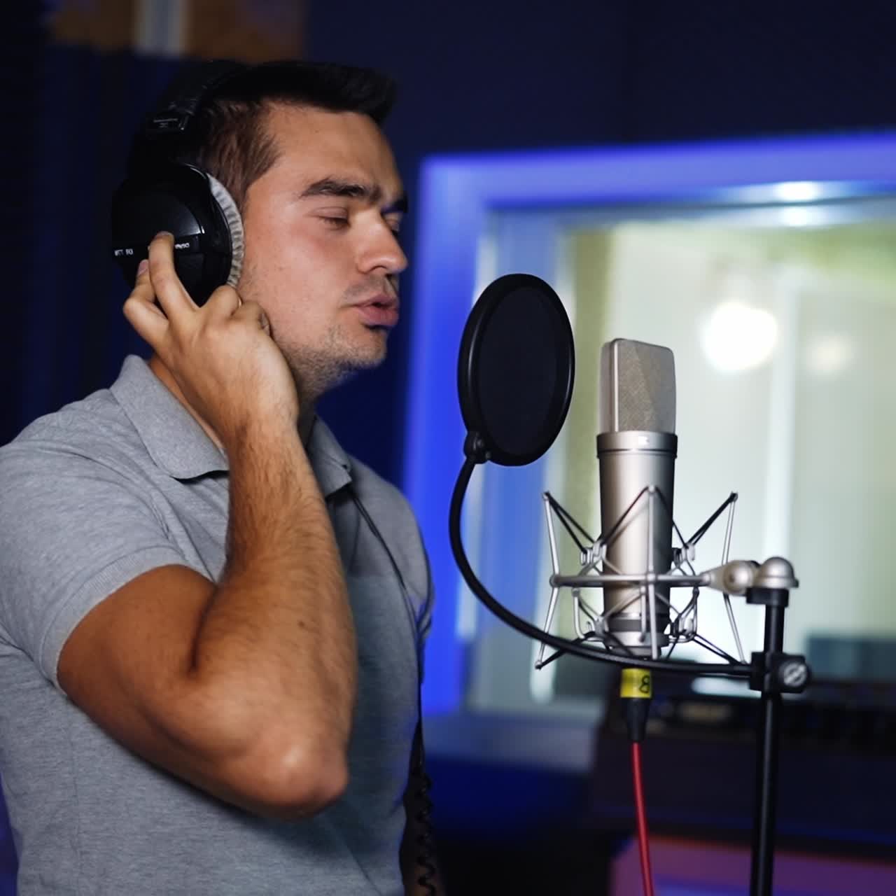 Male singer performing his song emotionally in studio. Man sings near the professional microphone holding his hand by the headphone