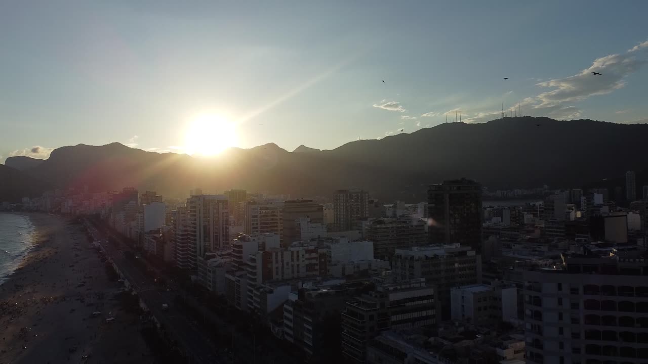 Sunset at Rio de Janeiro with birds flying in slow motion, Arpoador, with buildings and mounts backlit - aerial shot