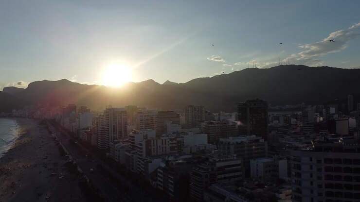 Sunset at Rio de Janeiro with birds flying in slow motion, Arpoador, with buildings and mounts backlit - aerial shot