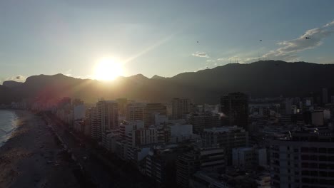 Puesta-De-Sol-En-Río-De-Janeiro-Con-Pájaros-Volando-En-Cámara-Lenta,-Arpoador,-Con-Edificios-Y-Monturas-Retroiluminadas---Toma-Aérea