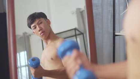 close up of a mirror showing asian teenager boy training with dumbbells while doing shirtless workout at home