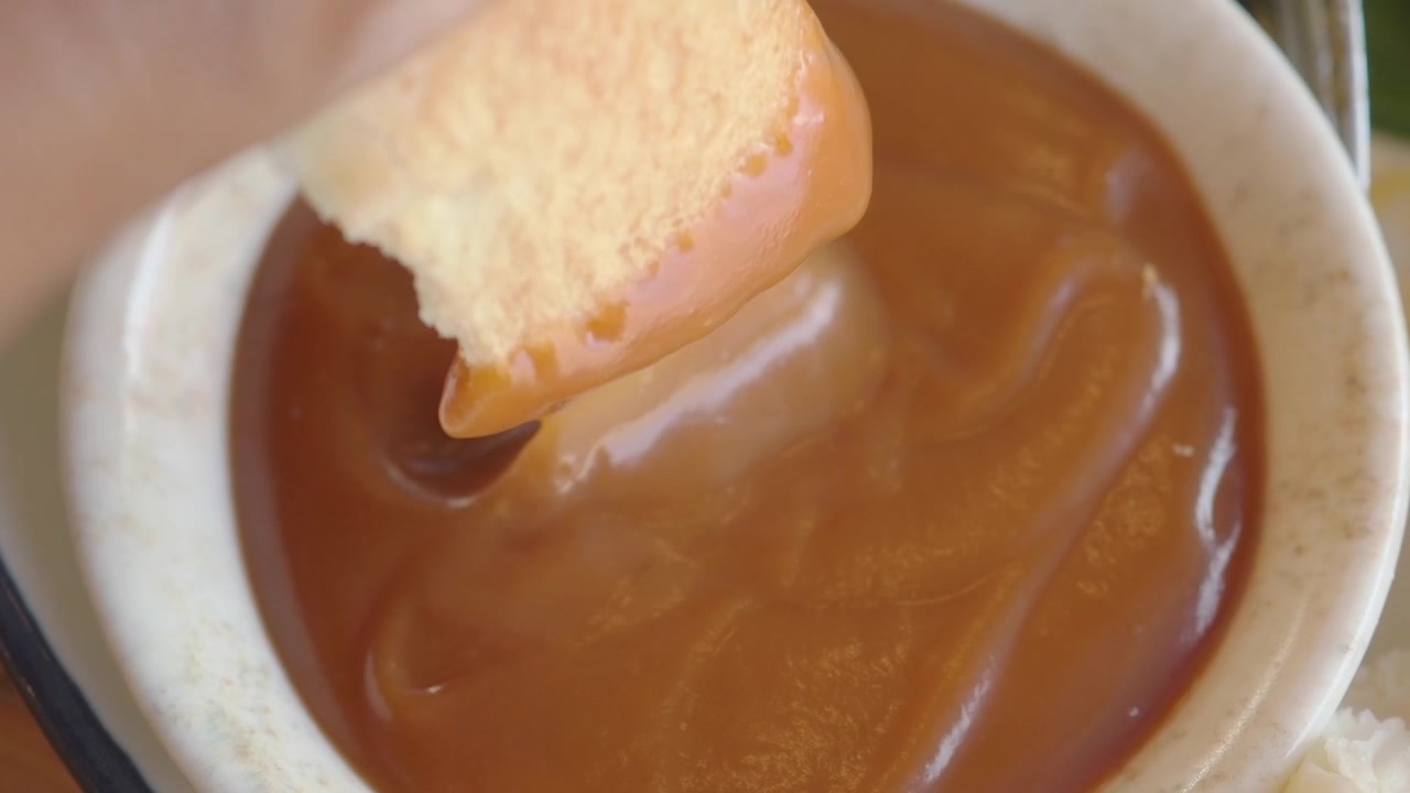 Primo piano di una mano che intinge il pane nella salsa dolce al caramello
