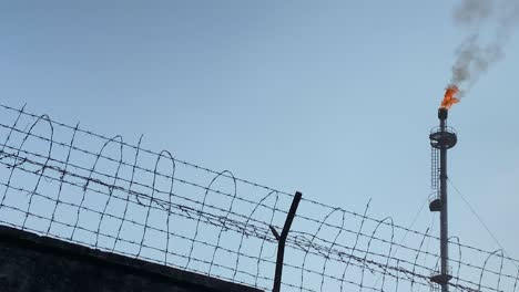 Low-angle-close-up-of-wired-fence-diving-industry-area-with-burning-Gas-Flare