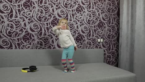 Little-happy-child-jumping-and-dancing-on-sofa-and-listening-music