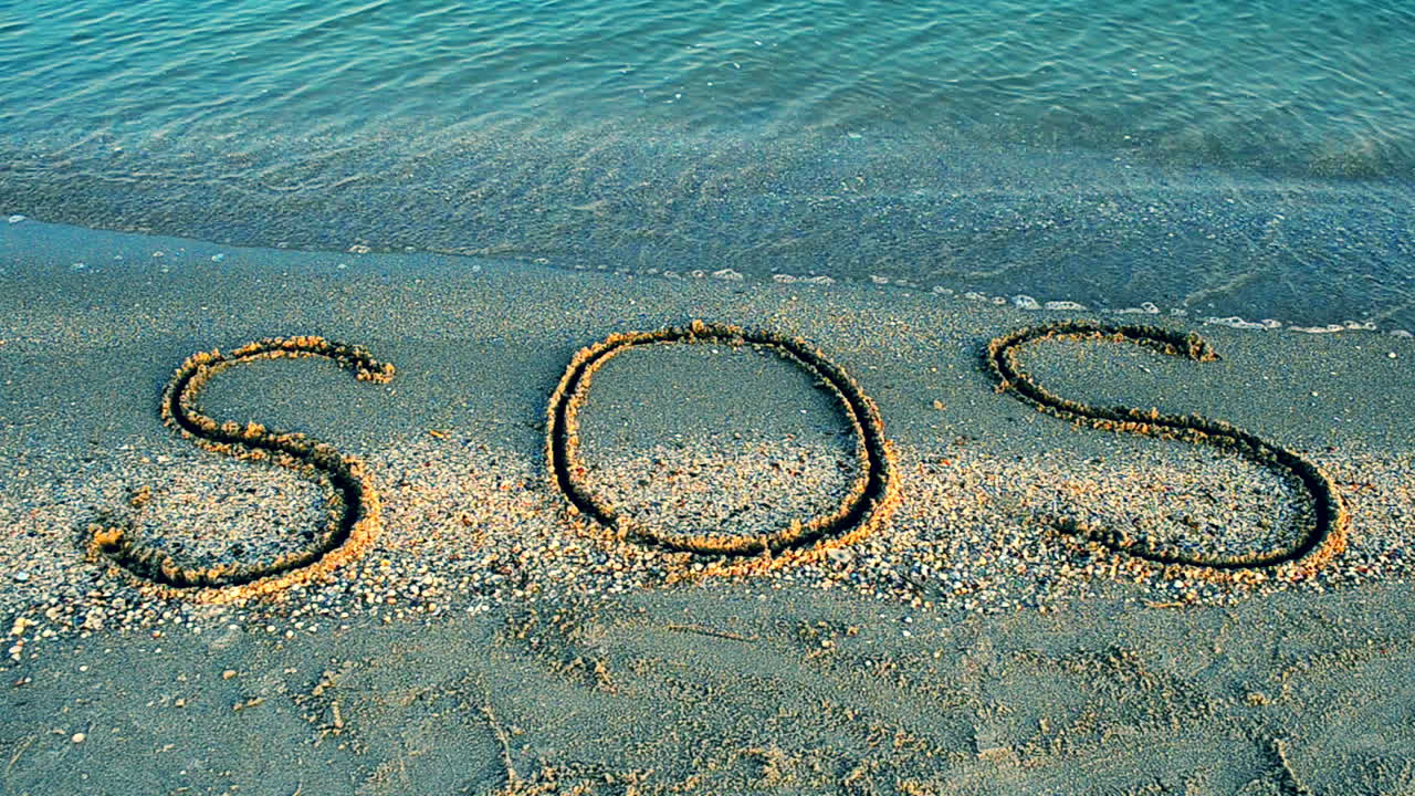 Inskriptionen SOS i sanden. Filmning på stranden