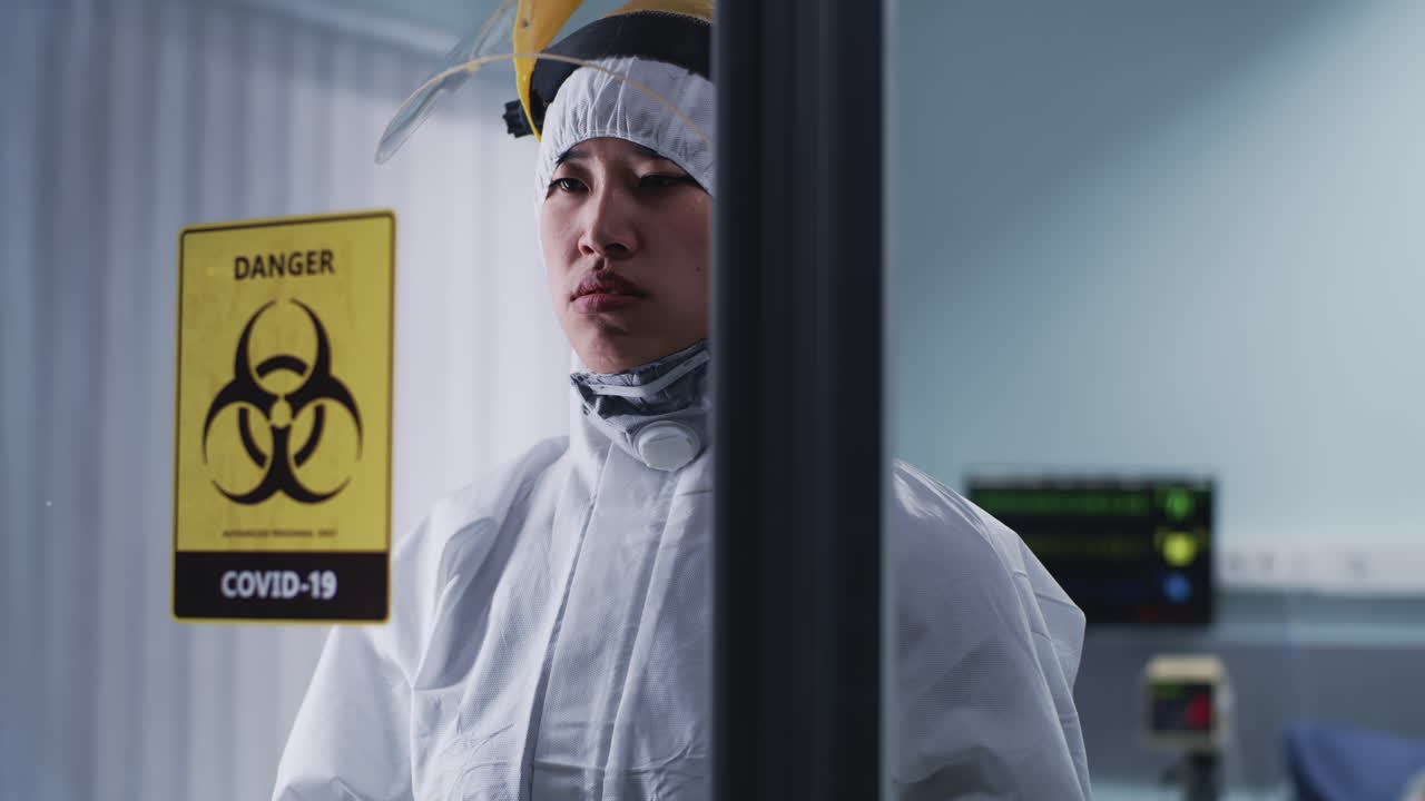 Healthcare Professional in Protective Suit Behind COVID-19 Biohazard Sign