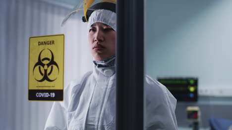 healthcare professional in protective suit behind covid-19 biohazard sign