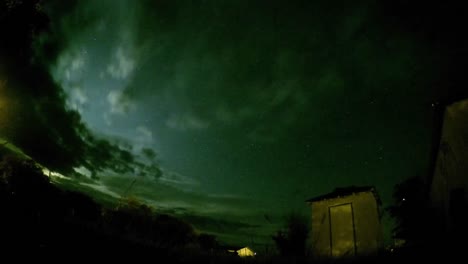 Lapso-De-Noche---Vista-De-Estrellas-Y-Nubes-En-Un-Campo-Con-árboles-Y-Una-Pequeña-Choza-Cerca