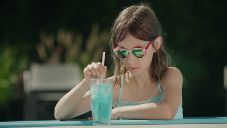 teenage girl crushes ice in a cocktail on the side of the pool