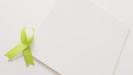 Video-of-pale-green-std-awareness-ribbon-and-white-card-with-copy-space,-on-white-background