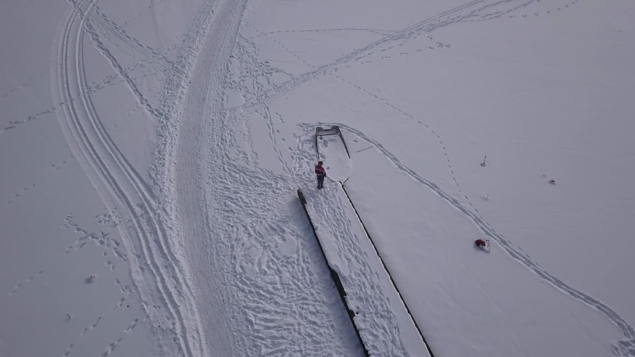 zoom suave en imágenes aéreas de una mujer parada cerca del final del embarcadero de madera en un lago congelado