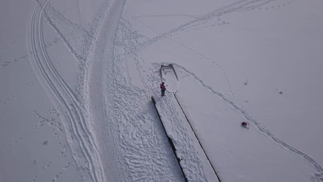 Smooth-zoom-in-aerial-footage-of-woman-standing-close-to-the-end-of-wooden-jetty-on-a-frozen-lake