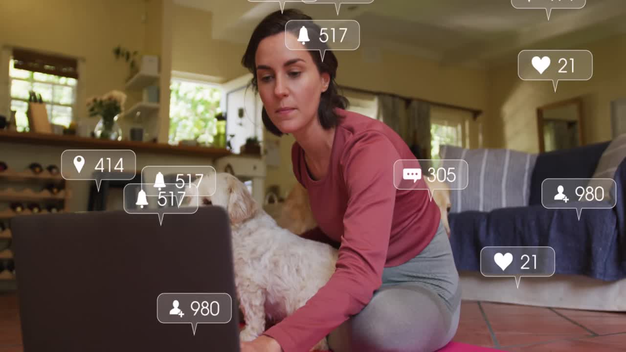 iconos digitales en burbujas de habla contra una mujer caucásica sentada con su perro usando una computadora portátil en casa