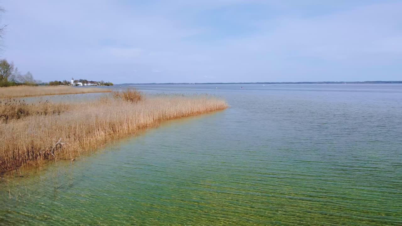 화창한 날 배경에는 아름다운 푸른 하늘, 맑고 푸른 물, 갈대, 알프스 산맥이 있는 시골 시골에 있는 바이에른의 유명한 호수 키엠제 위의 경치 좋은 낮은 비행