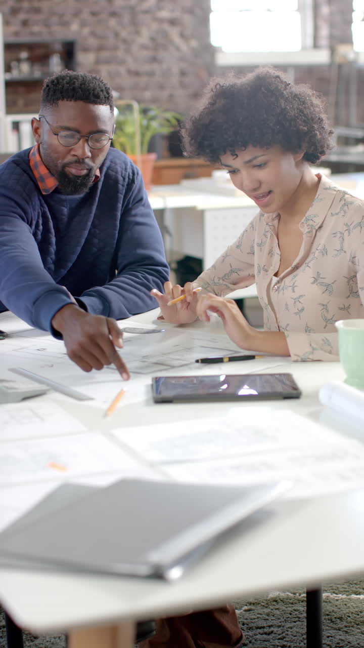 Vertical video of diverse colleagues discussing work with documents in office in slow motion