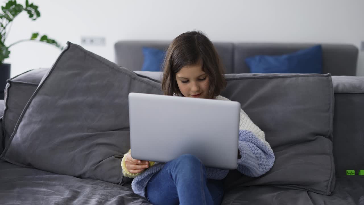 una niña de escuela usa una computadora portátil sentada en el sofá
