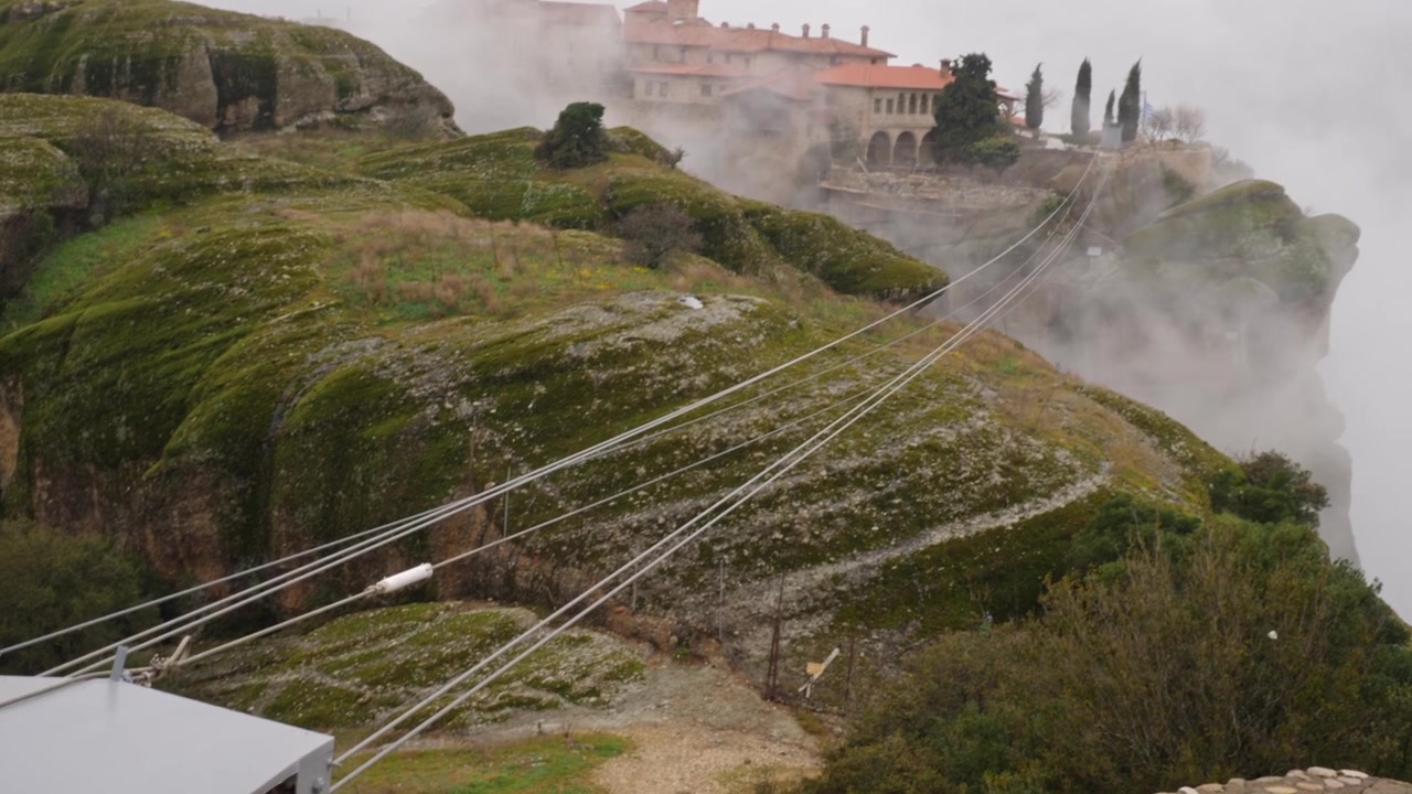 Meccanismo di risalita della funivia in funzione presso un monastero delle Meteore in Grecia. Una fitta nebbia mattutina avvolge l'antico complesso montuoso, creando un'atmosfera mistica e tranquilla