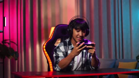 excited asian teen boy gamer playing video game on smartphone