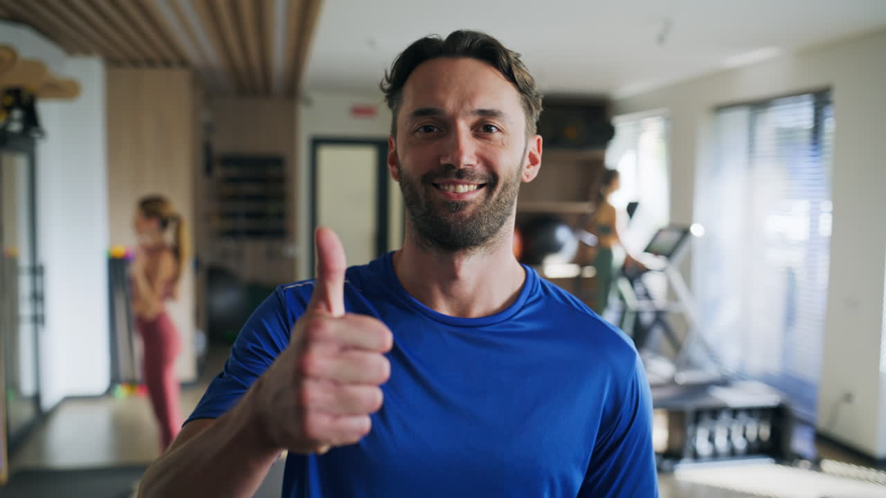 Primo piano di un uomo sorridente che fa il pollice in su in una palestra moderna. Sportivo positivo