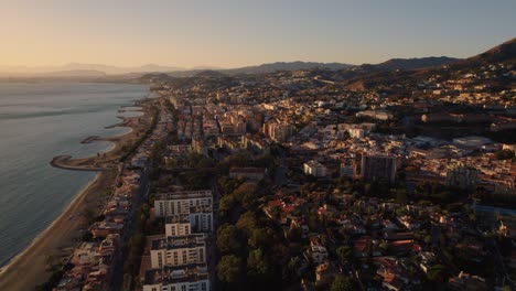 aerial forward moving drone shot over el candado beach in malaga spain with beautiful sunlight on seashore and beach houses