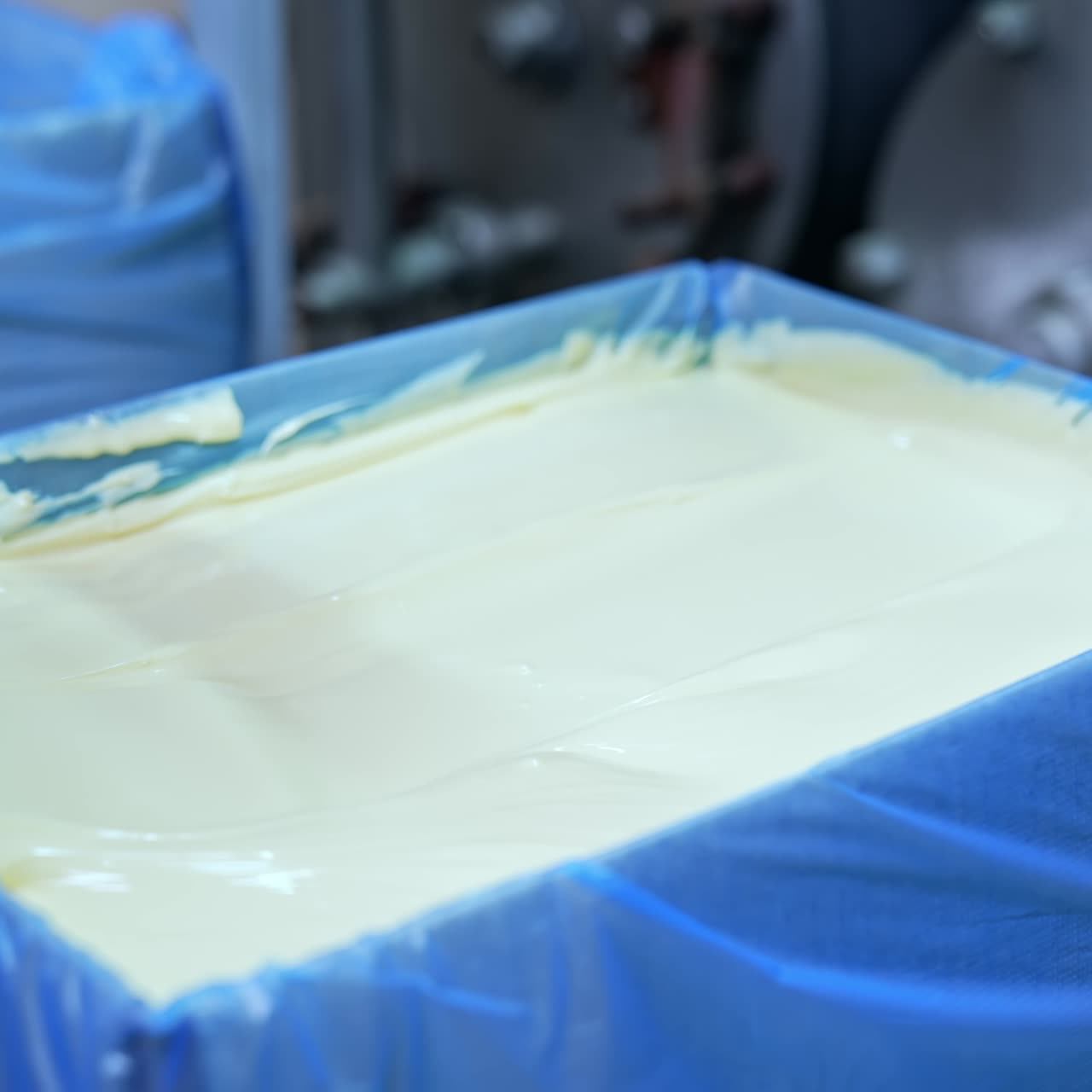 Smooth dairy product in a box. Production of fresh tasty butter on a milk farm. Worker levels the butter product in the container