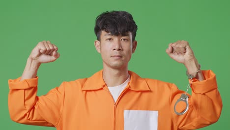 녹색 스크린 배경에 서서 팔꿈치를 구부리는 손이 부러진 아시아 남성 수감자의 클로즈업