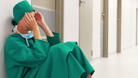 Tensed-female-surgeon-sitting-in-corridor