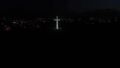 Aerial-drone-shot-approaching-a-glowing,-lit-cross-atop-a-hill-in-Nicosia-at-night