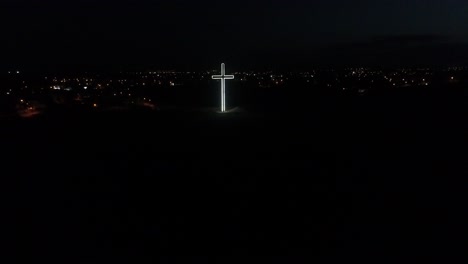 toma aérea de un dron acercándose a una cruz brillante e iluminada en la cima de una colina en nicosia por la noche