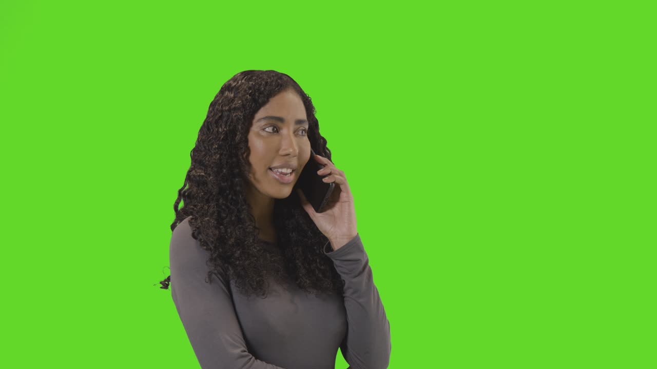 donna che parla al cellulare contro lo schermo verde sorridendo e ridendo