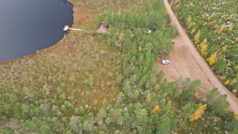 Vista-Aérea-De-Una-Autocaravana-Estacionada-En-Medio-De-Un-Bosque-De-Abetos-Cerca-De-La-Orilla-Del-Lago-En-Suecia