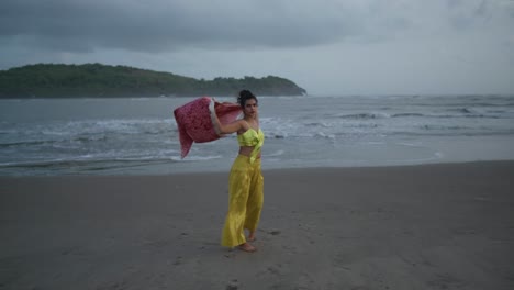 cinematic footage of indian fashion model wearing a yellow beautiful outfit and a red silk jacket on the beach in the wind in slow motion in goa india