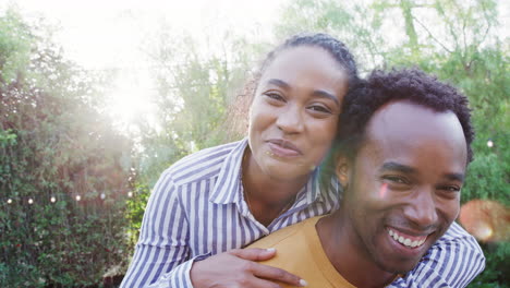 portrait of couple with man giving woman piggyback at home in back garden