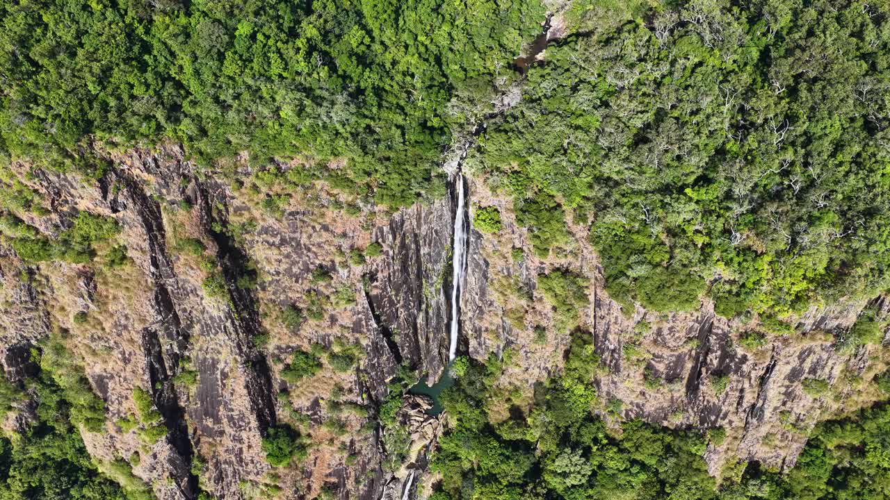 Drone footage captures a stunning waterfall cascading through lush greenery in the Daintree Rainforest, Port Douglas, Australia