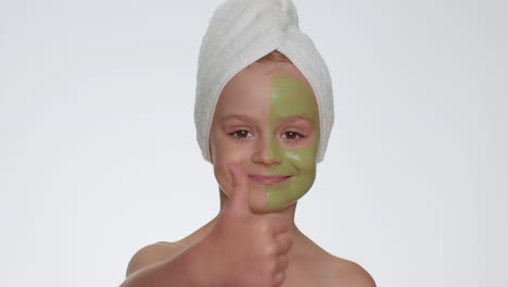 Beautiful-smiling-child-girl-kid-in-towel-on-head-applying-cleansing-moisturizing-green-mask-on-face
