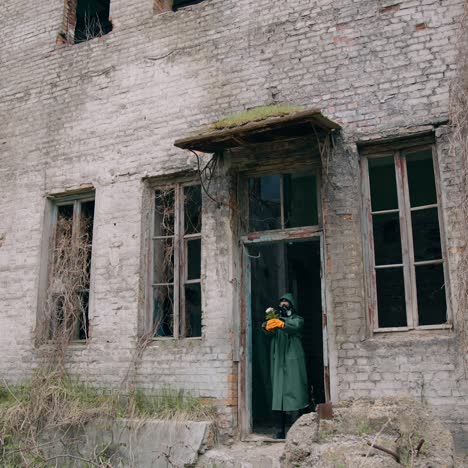 human in infected zone. ecologist in protective suit and gas mask coming out the abandoned building and holding flowers in hands