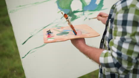 an artist, with a focus on their work, is seen holding a wooden palette filled with vibrant paint colors. wearing a checkered shirt, the virtuoso is carefully applying paint to a large canvas