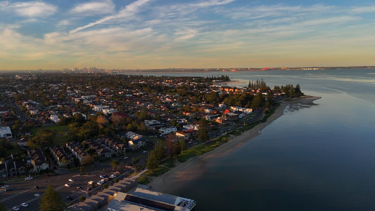 Aerial coastal town of Sardingham with beach, buildings, and harbor at golden hour, establishing panoramic, Sydney NSW Australia