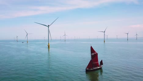 a flat bottomed sailing barge sailboat moves up the thames river estuary in england amidst numerous wind turbine windmills 3